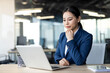 © Liubomir - Confident asian businesswoman wearing blue suit using laptop at office desk. Woman focused on work, reflecting professionalism, concentration. Modern office setting enhances productive atmosphere.