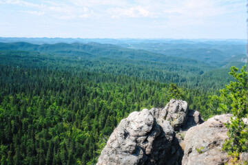 A scenic view from a rocky cliff overlooking a vast expanse of green forests and rolling hills, offering a serene and peaceful natural landscape. Generative AI