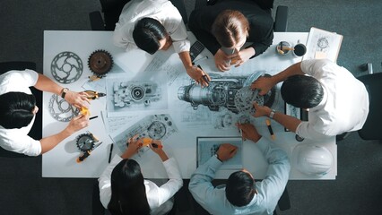 Top down aerial view of smart engineer team working together to design turbine engine. Professional technician discussing about jet engine construction while pointing at part of engine. Alimentation.