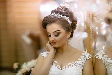 A woman in a wedding dress is wearing a tiara and is looking at the camera. She is in a reflective mood, possibly contemplating her upcoming wedding