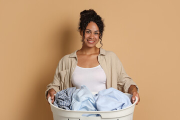 Wall Mural - Happy woman with basket full of laundry on beige background