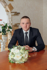 Wall Mural - A man in a suit and tie sits at a table with a bouquet of flowers in front of him