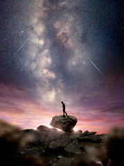 Wall Mural - a man standing on a rock as the milky way galaxy rises into the night sky at dusk. photo composite