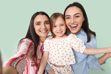 young lesbian couple with adopted little girl on green background, closeup