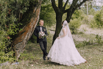 Wall Mural - A bride and groom stand in front of a tree, with the bride wearing a white dress and the groom wearing a suit