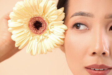 Poster - Beautiful Asian woman with flower on beige background, closeup