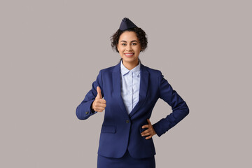 Canvas Print - Beautiful young African-American stewardess showing thumb-up on grey background