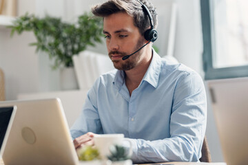 Business man doing video call with computer while talking with earphone sitting in modern startup office