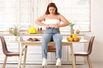 Wall Mural - Overweight young sad woman choosing between healthy and unhealthy food at home. Weight gain concept