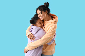 Poster - Happy young African-American woman with her daughter hugging on blue background