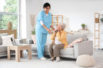 Wall Mural - Young African-American female medical worker helping elderly woman in nursing home