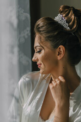 Wall Mural - A woman with a tiara on her head is looking at the camera. She is wearing a white robe and has her hand on her hip. Concept of elegance and sophistication