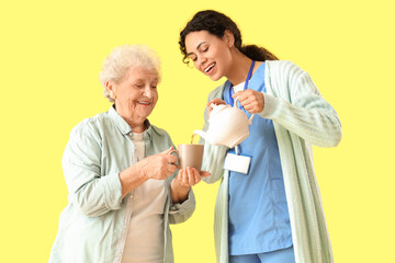 Sticker - Young African-American female medical worker pouring elderly woman cup of tea on yellow background