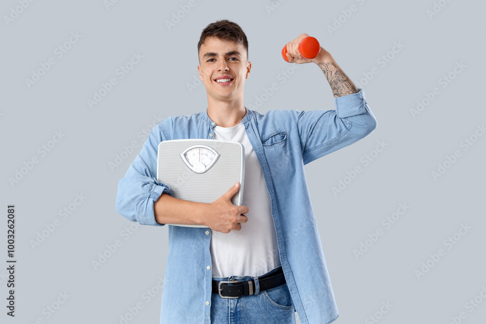 Young man with weight scales and dumbbell on light background