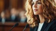 © Vuvimages - A focused woman is confidently speaking at a public event or meeting, captured from the waist up, emphasizing empowerment and communication in a formal setting.