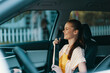 © SHOTPRIME STUDIO - Woman smiling inside a modern car, wearing a yellow dress and striped shirt, enjoying a sunny day, dashboard and steering wheel visible