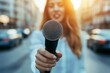 © zakiroff - Female reporter holding microphone on city street, sunshine background, journalism concept