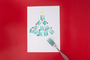 Wall Mural - Christmas tree craft using fork painting technique, green fir tree with yellow star and red ornaments on white paper, creative holiday project, unique texture, festive decoration, top view