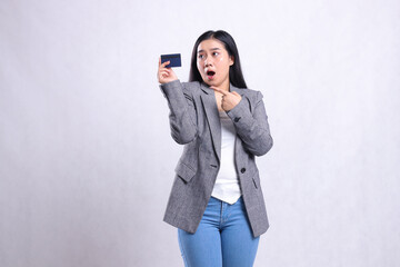 beautiful adult office female shocked looking, pointing and holding debit credit card wearing grey suit standing isolated on white background. for corporate, lifestyle, finance, transaction content