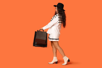 Poster - Beautiful young Asian woman with shopping bags on orange background