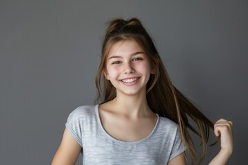 Smiling teenage girl on grey background. Adorable caucasian teenager with happy expression. Carefree and confident young girl in casual attire. Beautiful and cheerful portrait of teenage model.