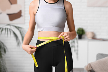 Canvas Print - Sporty young woman measuring her waist at home. Diet concept