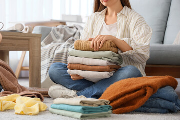 Poster - Young woman with stacks of clean clothes sitting on floor at home