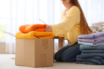 Poster - Young woman with tablet computer sorting stacks of clean clothes at home