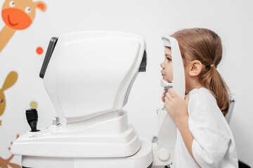 In a modern ophthalmology clinic, an ophthalmologist checks a little girl's vision using a binocular slit lamp. Advertisement for pediatric ophthalmology