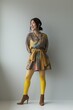 © miss irine - Smiling young Asian woman in fashionable clothing and yellow tights on grey background. She looks away with joyful expression. Brown boots and beret complete her outfit. Casual and trendy style.