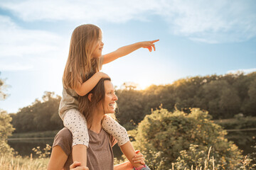 Mother and daughter exploring nature countryside together, mom giving her child piggyback at sunset, family lifestyle 