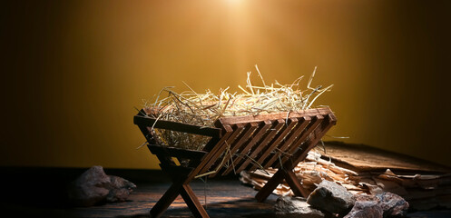 manger with hay, old book and stones on wooden table against dark color background
