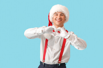 Poster - Young Santa Claus making heart gesture on blue background