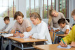 © JackF - Teenage boy and girl listening to teacher and writing exercises in notebook at lesson in secondary school
