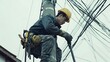 © Hesti - A utility worker in a yellow hard hat and blue work clothes climbs a pole and fixes a cable, with many other cables around him.