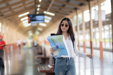 Young woman female smiling traveler with back pack looking to map while waiting for the train at train station, A woman is standing at a train station with a map in her hand