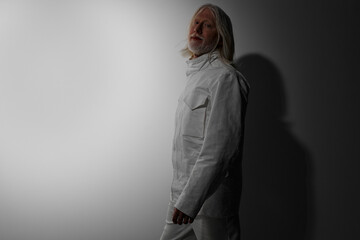 Fashion model in a stylish white outfit standing against a dark background with soft lighting, exuding a modern and minimalistic vibe