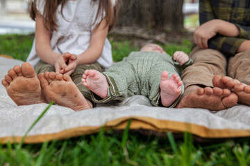 three children with dirty feet sitting on a blanket outdoors