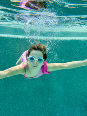 Girl swimming underwater in a pool wearing goggles and a pink swimsuit