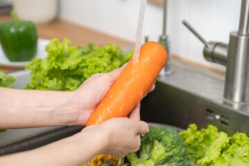 Close up asian young woman washing carrot, tomato, broccoli  fresh vegetables, paprika with splash water in basin of water on sink in kitchen, preparing fresh salad, cooking meal. Healthy food people.