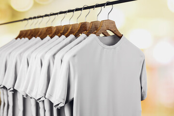 Canvas Print - Row of empty white t-shirts hanging on rack on blurry light bokeh background. Mock up place. Fashion and showroom concept. 3D Rendering.