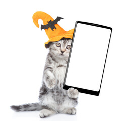 Poster - Cute kitten wearing hat for halloween holds shows smartphone with white blank screen in it paw. Isolated on white background