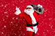© deagreez - Hip-hop miracle. Full length photo of retired old man grey beard smile hold boombox direct finger empty space wear santa x-mas costume sunglass headwear isolated red color background