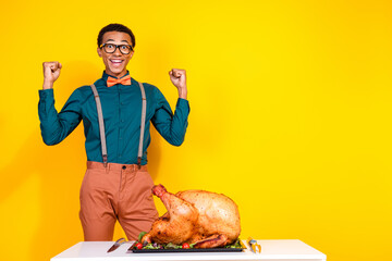 Portrait of elegant young man raise fists roasted thanksgiving day turkey empty space isolated on yellow color background