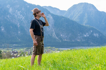 Wall Mural - An elderly Tyrolean man, 50-55 years old, wearing traditional clothes, sings and shouts against the backdrop of a village surrounded by mountains, 