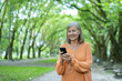 © Liubomir - Smiling mature woman enjoying music on smartphone while walking in park. Wearing earphones, feeling relaxed and content. Casual outdoor setting reflecting enjoyment and tranquility.