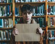 © Bussakon - Student Holding Cardboard Sign With Deep Focus and Contemplation in Library