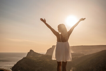 Wall Mural - A woman is standing on a hill overlooking a body of water. She is wearing a white dress and she is happy.