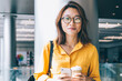 © BullRun - Half length portrait of attractive female blogger in optical spectacles for provide eyes protection smiling at camera during coffee break for networking with cellphone gadget, millennial person