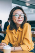 © BullRun - Portrait of cheerful hipster girl in optical spectacles for provide eyes protection looking at camera and smiling during blogging time in university classroom, concept of browsing and networking